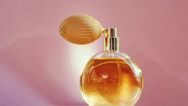 Luxury golden perfume bottle and shining light flares on pink background, glamorous fragrance scent as perfumery product for cosmetic and beauty brand, stock footage