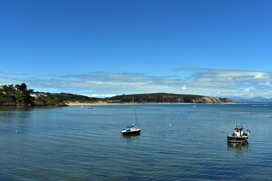 Two boats in the bay at the beautiful Welsh seaside resort of Abersoch.  Calm sea waters with reflections from the boats and the pine clad cliffs.  Blue sky with distant cloud.  Copy space.