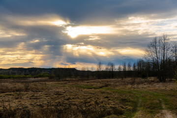 Fototapeta na wymiar Clouding sunset in a field in a village in Belarus. Evening time in the field. The sun behind the clouds. The sun through the clouds. Shining sky.