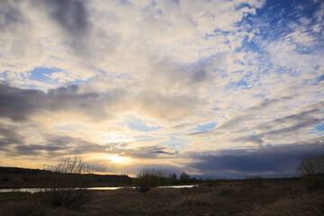 Clouding sunset in a field in a village in Belarus. Evening time in the field. The sun behind the clouds. The sun through the clouds. Shining sky.