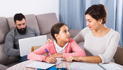 Young woman helping her daughter to prepare homework at home