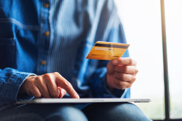 Closeup image of a woman holding credit card while using tablet pc