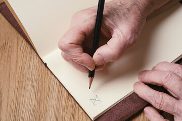 Closeup wrinkled hands of a person writing. Elderly woman's hands holding a pencil and  puts a...