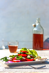Summer breakfast. Vegan salad plate of tomatoes, cucumbers, onion and tofu. Bottle and glass of refreshing red drink or wine in background. Selective focus.