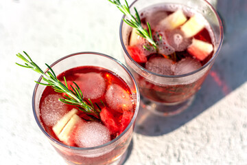 Two glasses with red refreshing summer drink or red wine, ice cube, pieces of watermelon and rosemary sprigs. Summertime concept. Top view. Selective focus.