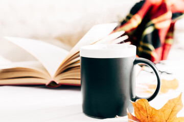Autumn cozy composition. Plaid, steaming cup of hot chocolate, book, autumn leaves. Autumn or winter concept of coziness and interior. Front view, copy space