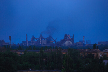 Panorama of a large metallurgical plant that smokes heavily on the outskirts of the city in the evening