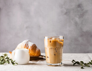 Cold black coffee with ice cubes in tall glass and fresh croissant. Refreshing coffee drink on a...