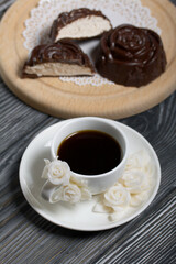 A cup of black coffee on a saucer. Nearby zephyr in chocolate. Zephyr in the form of a rose. One zephyr is cut in half, a slice is visible.
