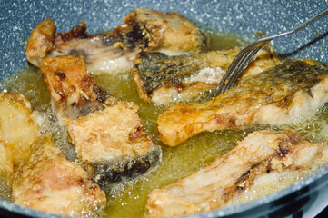 close-up - almost cooked pieces of fish, fried in a pan, checked with a fork