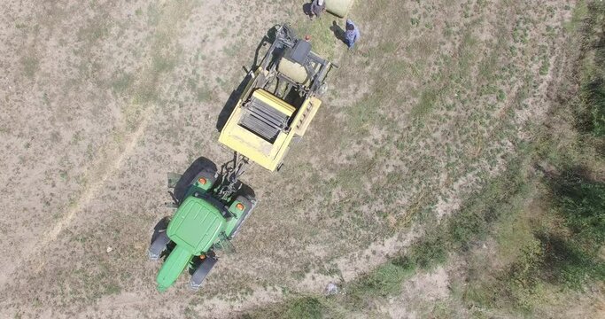 Tractor and field agriculture round baler for animal feed, discharges a wheat baler during harvesting. Aerial shot of bird eye view