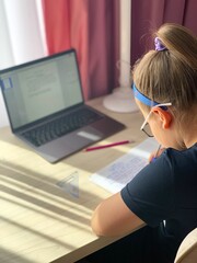 Brunette girl doing lessons on the computer. Home study on self-isolation, for the schoolboy. Office on a table for the pupil.