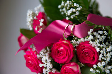 Close-up, gold wedding rings on a pink satin ribbon lying on the bride's beautiful wedding bouquet