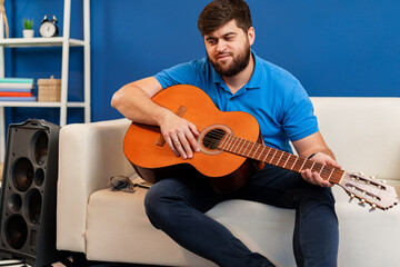 Young man guitar player sitting and performing on a couch