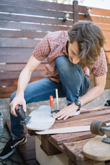 Attractive man polishing wooden deck for skateboard. Portrait of male worker holding power sander and polishing wooden board.