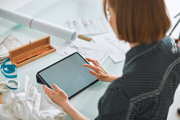 Young girl fashion designer works on tablet with empty screen in workshop. Photo for ad educational courses or clothing