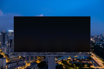 Blank black road billboard with Kuala Lumpur cityscape background at night time. Street advertising poster, mock up, 3D rendering. Front view. Concept of marketing to promote or sell idea or product.