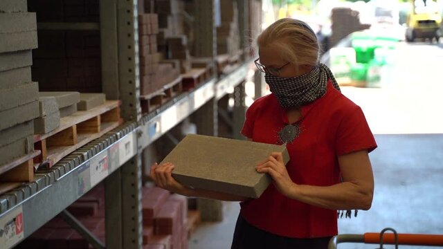 Woman wearing a face covering looking at concrete brick pavers in a hardware store.