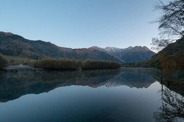 Fototapeta na wymiar 紅葉の上高地・大正池から見た朝日に照らされる穂高連峰