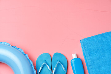 Beach concept with blue rubber ring, towel, flip-flops and moistrizer on pink background