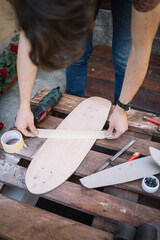Man sticking paper tape on wooden board. Cropped man attaching tape to skateboard on wooden pallet with power sander and tools.
