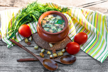 Delicious broth with croutons, dill, tomatoes on an old wooden background. Lunch with soup in a clay pot vegetarian in the open air.