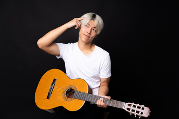 Young asian man with guitar over black background having doubts and with confuse face expression