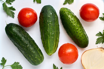 Three cucumbers, three tomatoes, half an onion and parsley with drops of water on a white background.