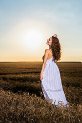 A beautiful woman in a white dress in a wheat field at sunset.