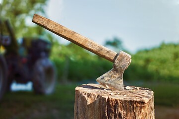 An ax sticking out of the deck. On a blurred background tractor, green plants and sky.