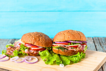 Sandwiches with lettuce, bacon, onion rings, tomatoes, egg, cheese and sesame bun on a light blue background. Copy space.