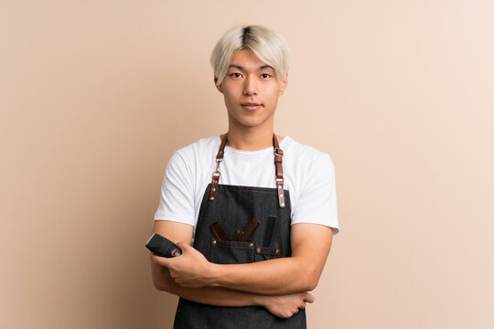 Young Asian Man Over Isolated Background With Hairdresser Or Barber Dress And Holding Hair Cutting Machine