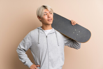 Young asian man over isolated background with skate and looking side © luismolinero