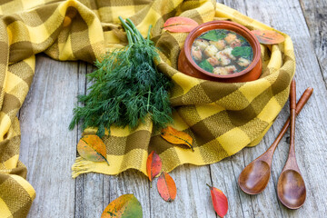 Autumn soup with croutons and dill is warmed wrapped in a scarf with fallen yellow leaves lying around.