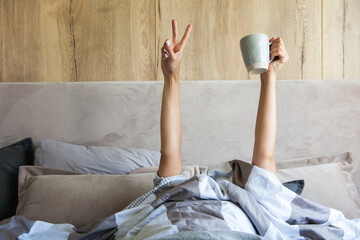 Woman's hand with a cup of coffee in bed, the concept of the beginning of a new day, good morning