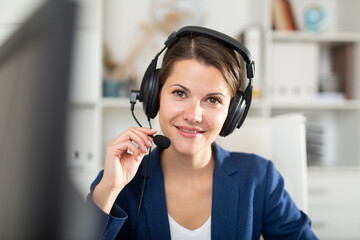 Portrait of smiling young woman helpline operator with headphones during work in call center