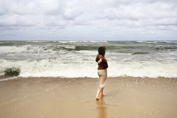 young woman walking on the beach and looking at the sea with a tide and waves