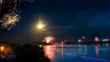 Fireworks over a lake with a full moon shining, lights reflected upon the water, shine the light.