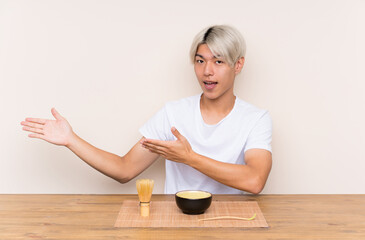 Obraz na płótnie Canvas Young asian man with matcha tea in a table extending hands to the side for inviting to come