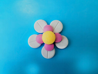 Pharmaceutical pills flowery pattern, isolated on blue, closeup of capsules of medicine, medical concept.