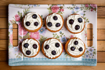Homemade blueberry cup cake decorated with white cream and three blueberries lactose-free dessert, on natural wood

