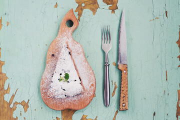 Piece of berry pie on cutting board, fork, knife on old painted wooden background.