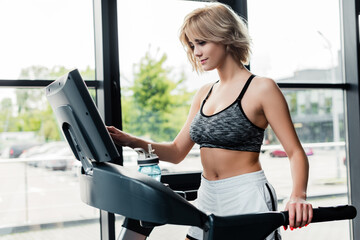 Fototapeta premium attractive sportswoman touching screen on modern treadmill