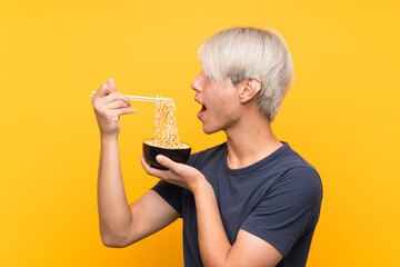 Young asian man with noodles over isolated yellow background