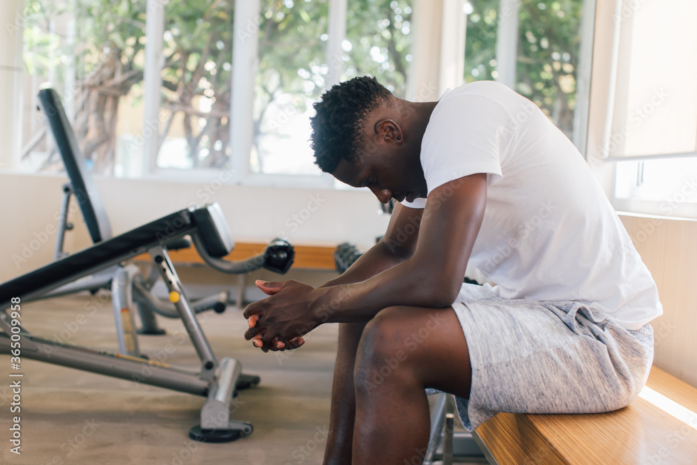 Wall mural desperate african american male athlete sitting on bench during break in fitness training in modern 