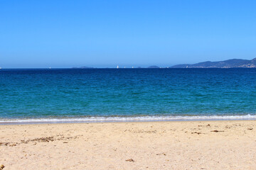 Fototapeta na wymiar blue sea over sand beach with boats and city behind