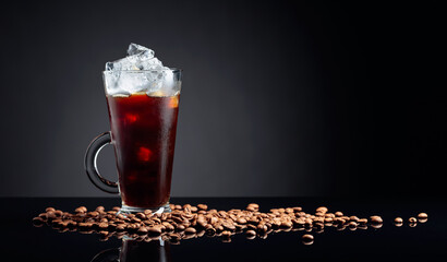 Ice coffee in frozen glass and coffee beans on a black reflective background.