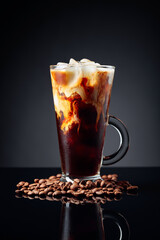 Ice coffee in frozen glass and coffee beans on a black reflective background.