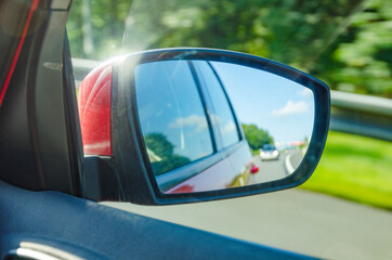 Reflection of blurred car in the rearview mirror on highway in beautiful sunny day