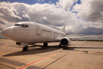 A white plane stands on the airport platform near the runway. Layout, place for text. Copy space. Sky clouds.
